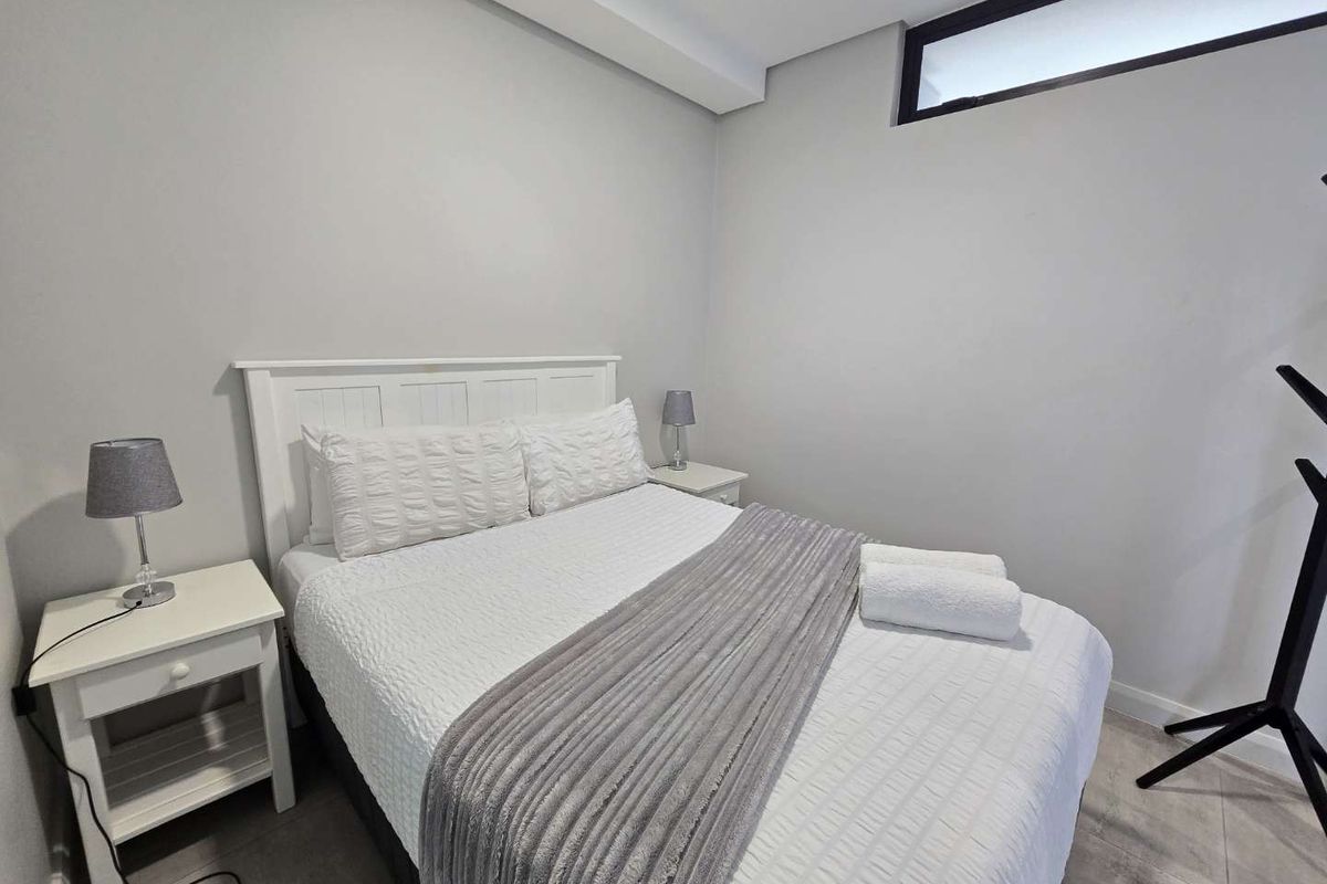 A well-maintained bedroom featuring neutral wall tones, tiled flooring, and a high-positioned clerestory window for natural light.