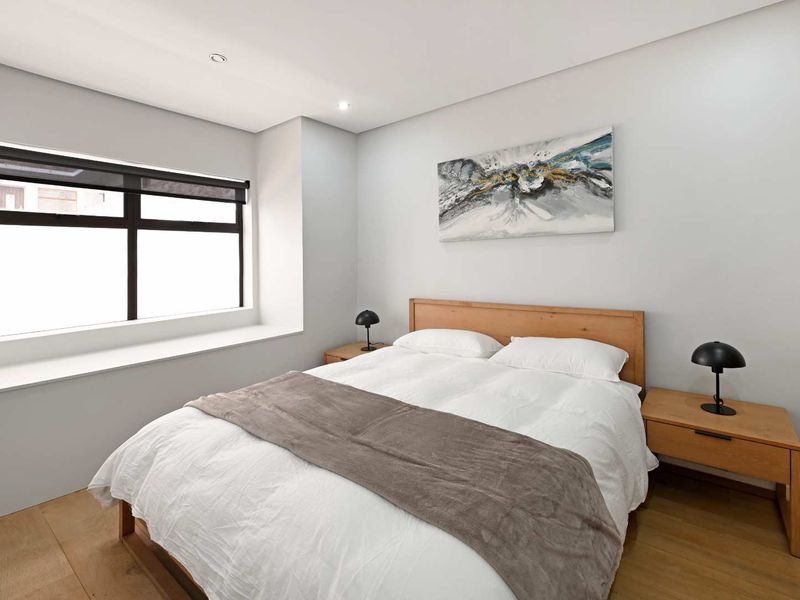 A well-maintained bedroom featuring modern recessed downlights, timber flooring, and a large window with a sleek black frame.