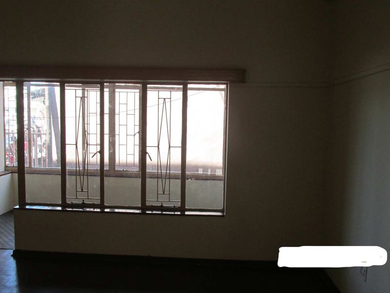An empty living room featuring large windows with integrated metal security bars and timber frames, offering a blank canvas for potential interior updates.