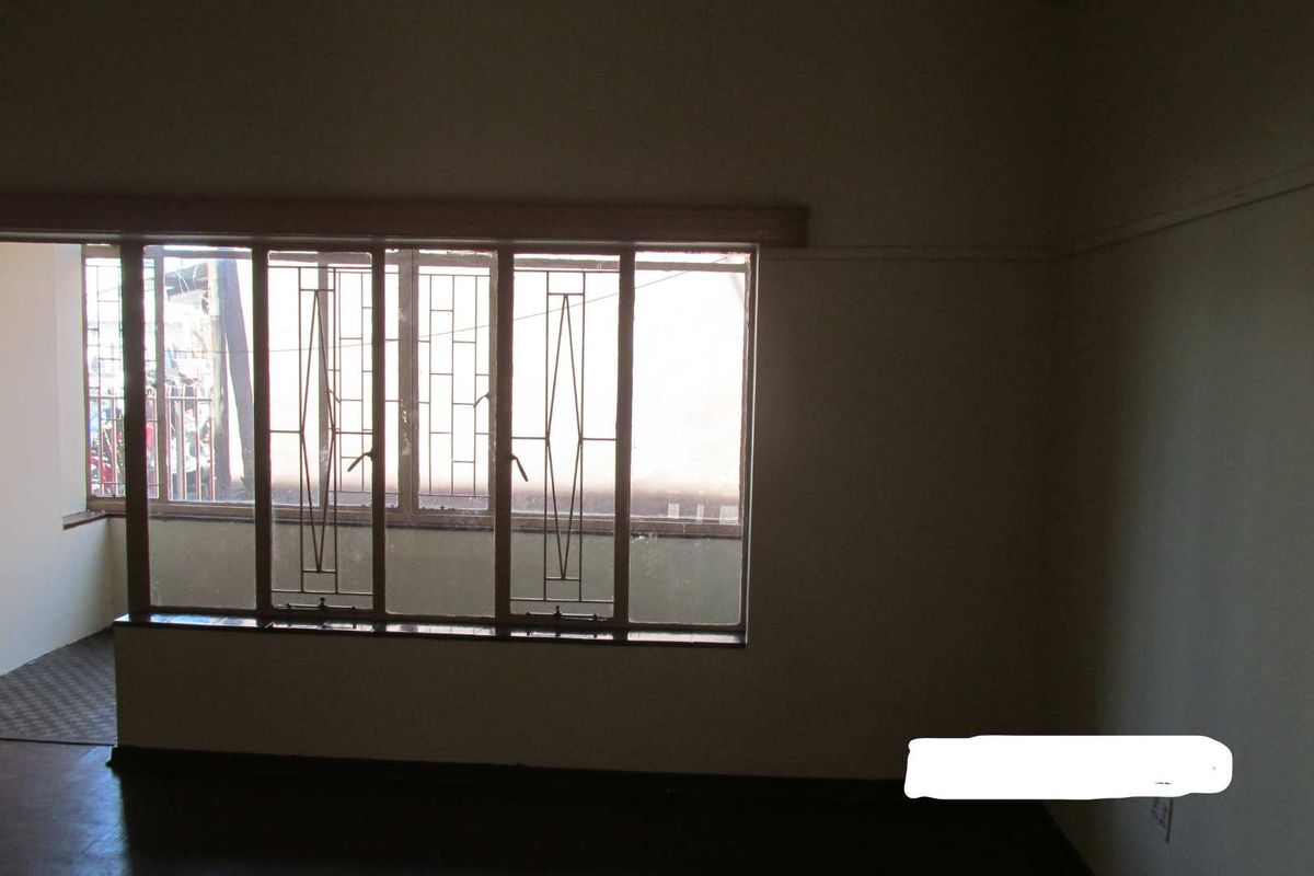 An empty living room featuring large windows with integrated metal security bars and timber frames, offering a blank canvas for potential interior updates.