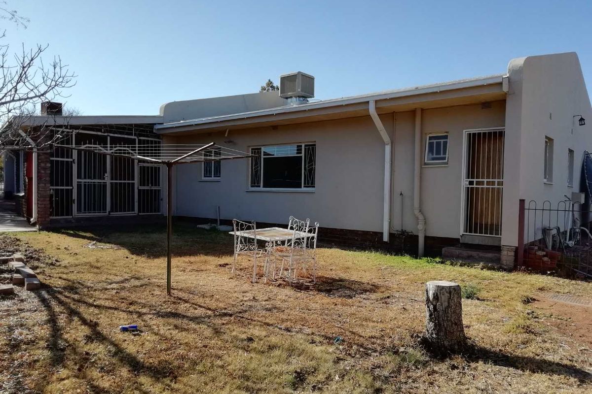 Rear view of the property featuring a spacious backyard, exterior wall finishes, security gates, and a roof-mounted evaporative cooling unit.