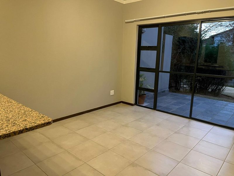 An empty open-plan living area featuring neutral tiled flooring, a granite breakfast bar, and large sliding glass doors leading to an outdoor patio.