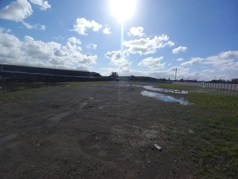 A large, undeveloped industrial plot featuring unpaved ground and perimeter fencing, suitable for future development or storage.