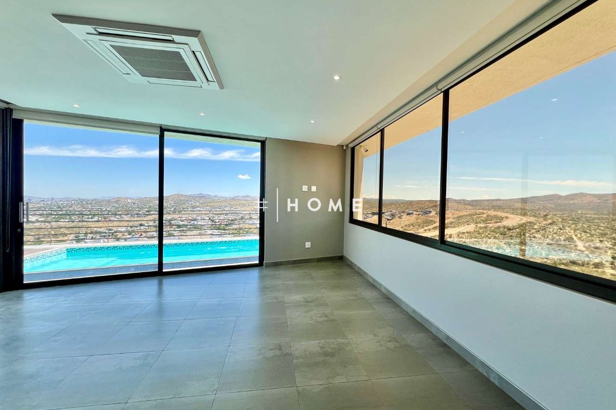 Spacious living area featuring large floor-to-ceiling sliding glass doors, recessed ceiling lighting, integrated air conditioning, and expansive panoramic views of the surrounding landscape.