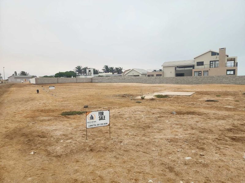 A vacant residential plot featuring a level sandy surface, boundary walling, and an existing concrete slab, ready for new development.