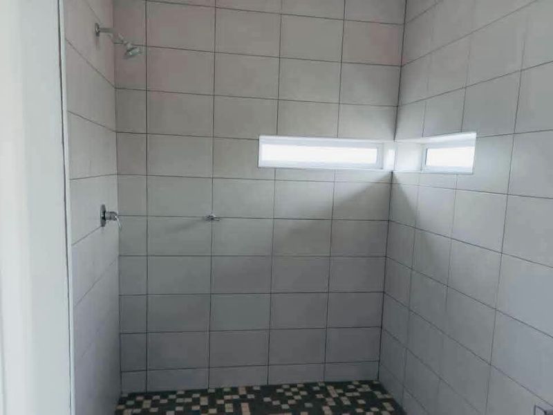 A clean, modern shower enclosure featuring neutral wall tiles, a patterned floor, and a corner window for natural light.
