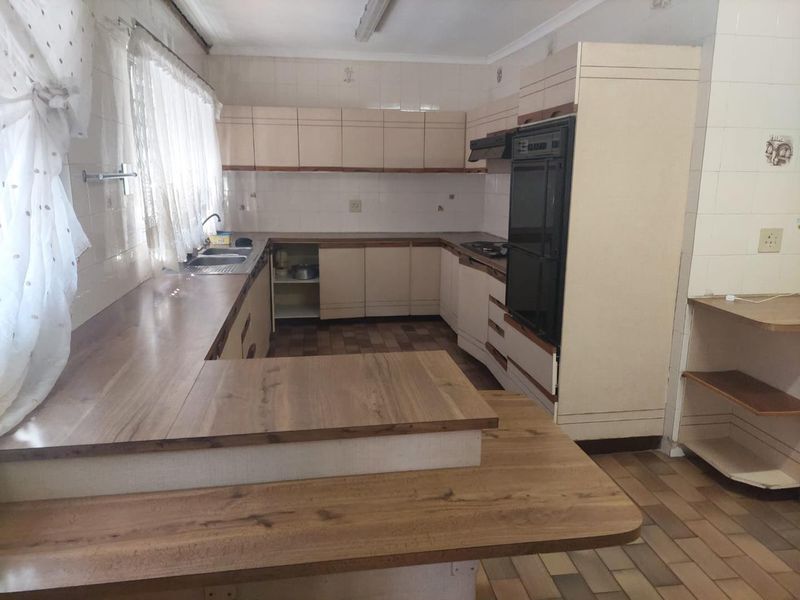 A dated kitchen featuring built-in cabinetry, laminate countertops, a double sink, and integrated oven and hob, offering significant potential for modernization.