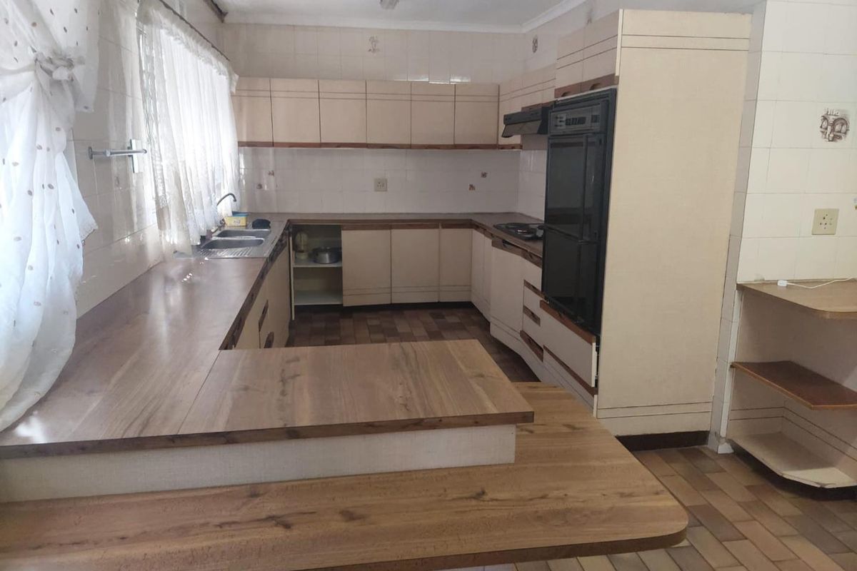 A dated kitchen featuring built-in cabinetry, laminate countertops, a double sink, and integrated oven and hob, offering significant potential for modernization.
