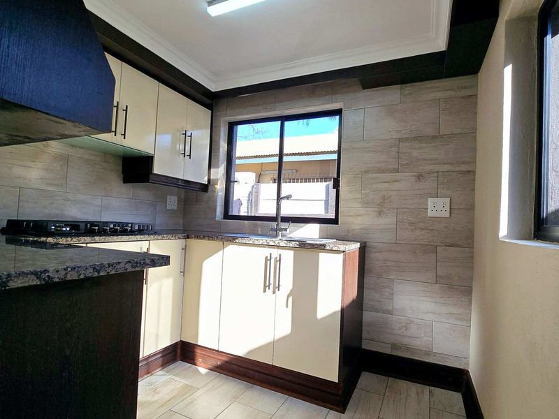 A modern, well-maintained kitchen featuring granite countertops, built-in cabinetry, a hob with extractor fan, and neutral tiled finishes throughout.