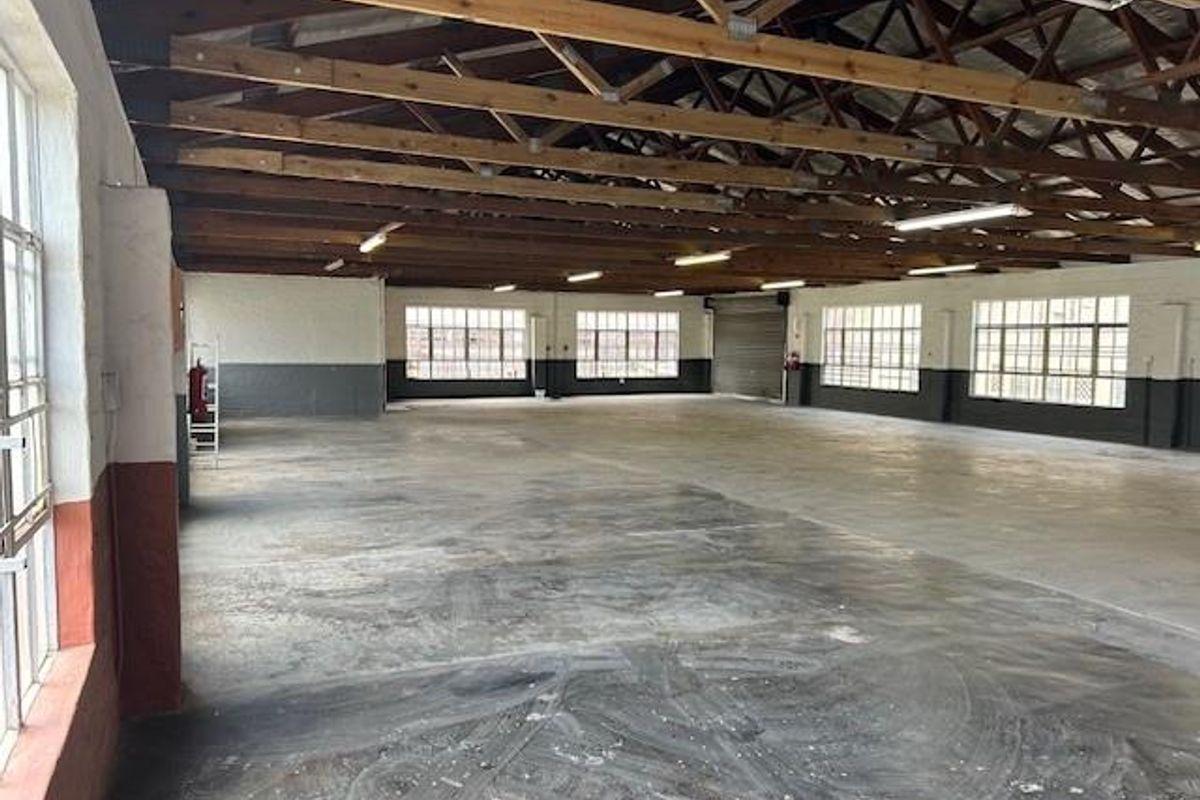 Spacious industrial warehouse area featuring exposed timber roof trusses, concrete flooring, and large steel-framed windows providing ample natural light.