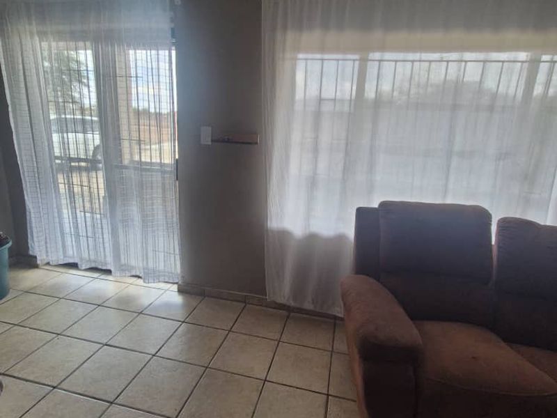 A living room area featuring tiled flooring, large windows with security bars, and a sliding glass door providing access to the exterior.