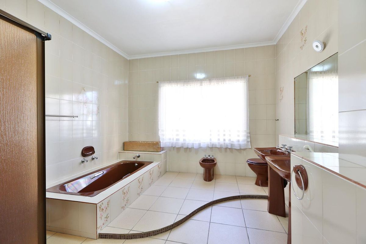 Spacious bathroom featuring a dated brown suite, including a built-in bathtub, bidet, toilet, and pedestal basin with neutral wall tiling.