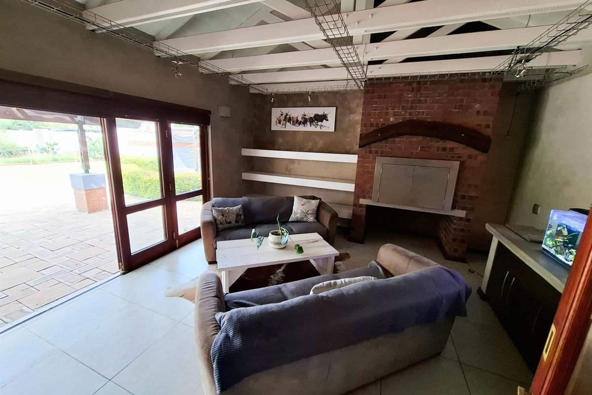 Spacious living area featuring exposed timber ceiling beams, a rustic brick fireplace, built-in shelving, and large sliding glass doors opening to the patio.
