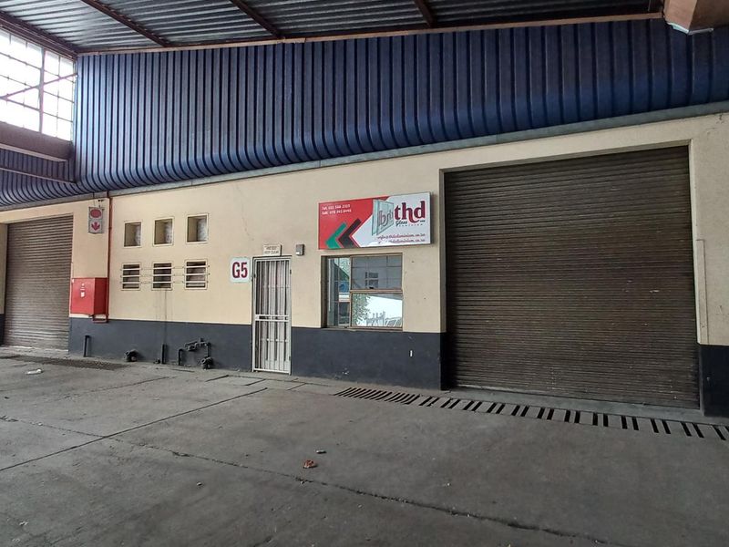 Industrial unit exterior featuring large roller shutter doors, concrete flooring, and a high-clearance metal roof structure.