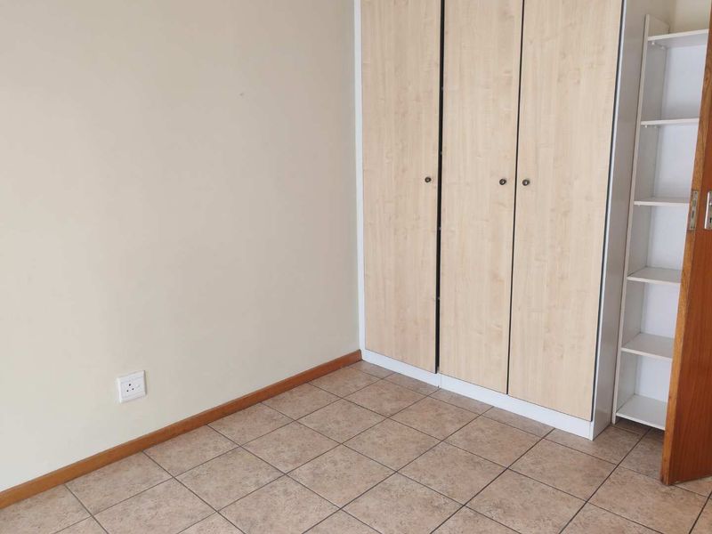 A clean, empty bedroom featuring neutral walls, tiled flooring, and built-in wooden cupboards, offering a versatile space ready for personalization.
