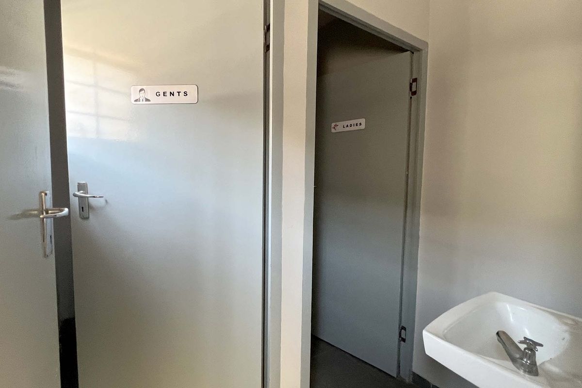 A functional industrial restroom area featuring separate Gents and Ladies facilities with a wall-mounted basin.
