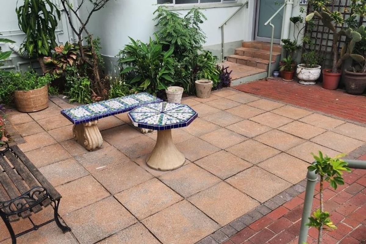 A paved rear courtyard area featuring brick borders, external stairs leading to an entrance, and established garden greenery.