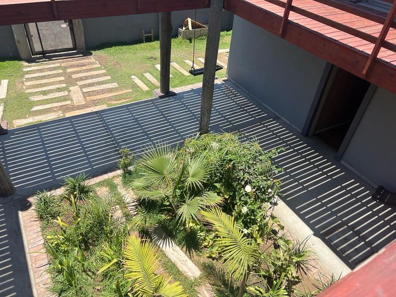 An elevated view of a rear courtyard featuring a wooden deck, timber support posts, and a landscaped garden area with brick edging.