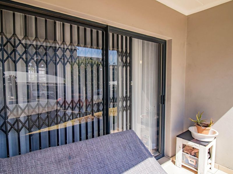 A covered balcony area featuring tiled flooring, a sliding glass door, and a fitted security gate for added protection.