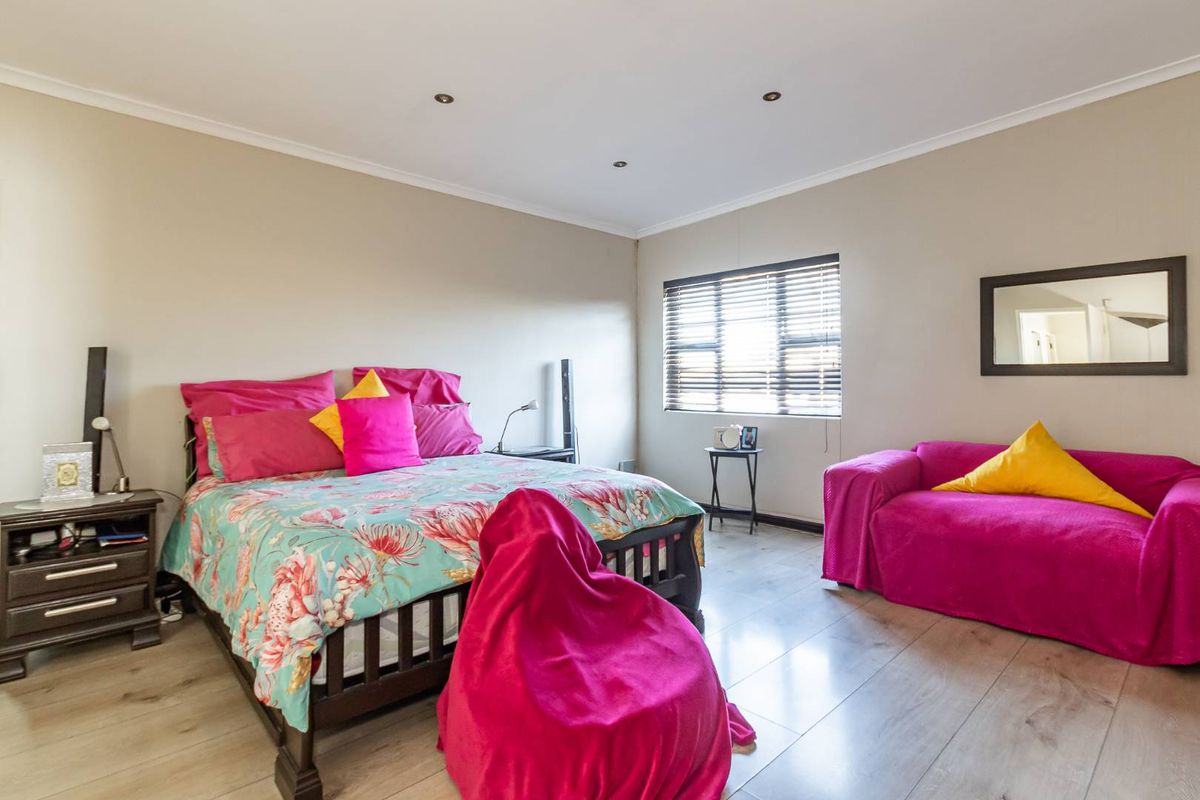 A well-lit bedroom featuring light-toned laminate flooring, recessed ceiling downlights, and venetian blinds, offering a neutral base for interior design.