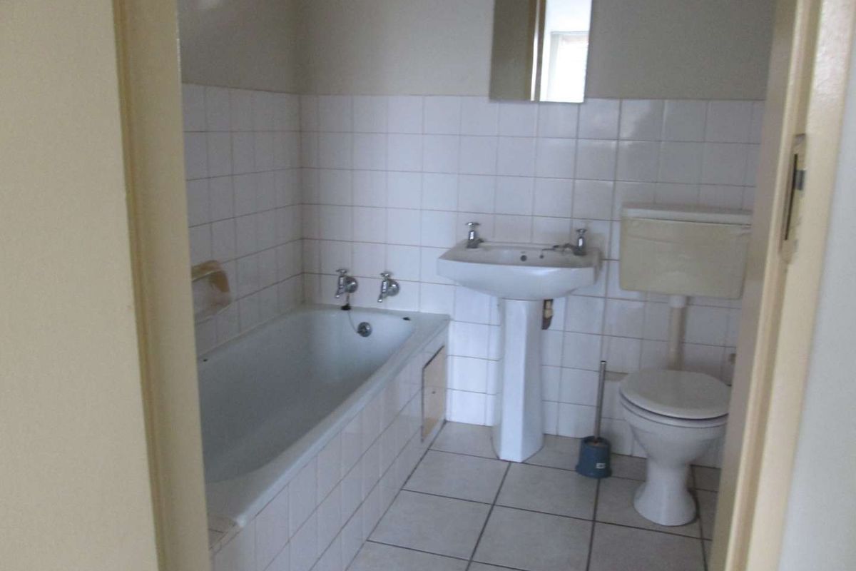 A functional bathroom featuring a standard bathtub, pedestal basin, and toilet with white wall tiling and tiled flooring.
