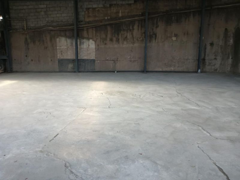 An empty industrial utility space featuring exposed concrete block walls, steel structural columns, and a concrete floor with visible surface cracking.