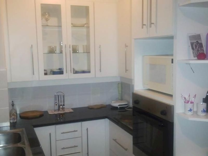 A compact kitchen featuring white cabinetry, black granite countertops, a built-in oven, and a stainless steel double sink with a tiled backsplash.