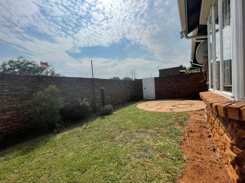 A private rear garden featuring a brick boundary wall with electric fencing, a small lawn area, and a circular paved patio.