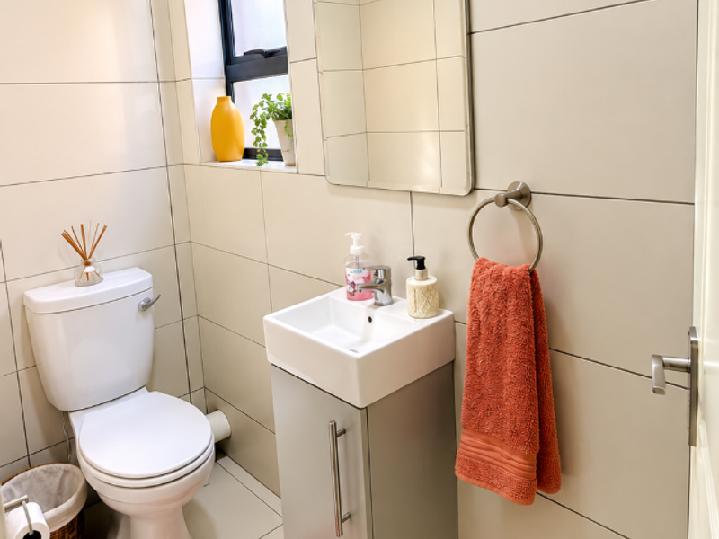 A compact, modern guest bathroom featuring floor-to-ceiling wall tiles, a wall-mounted vanity with basin, and a standard toilet.
