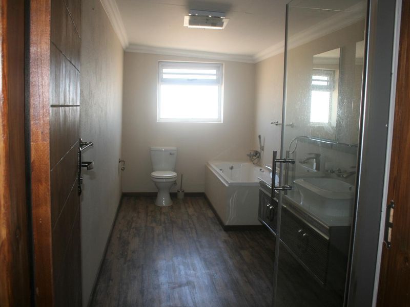 A clean, modern bathroom featuring a built-in vanity, bathtub, toilet, and a glass-enclosed shower with wood-look laminate flooring.