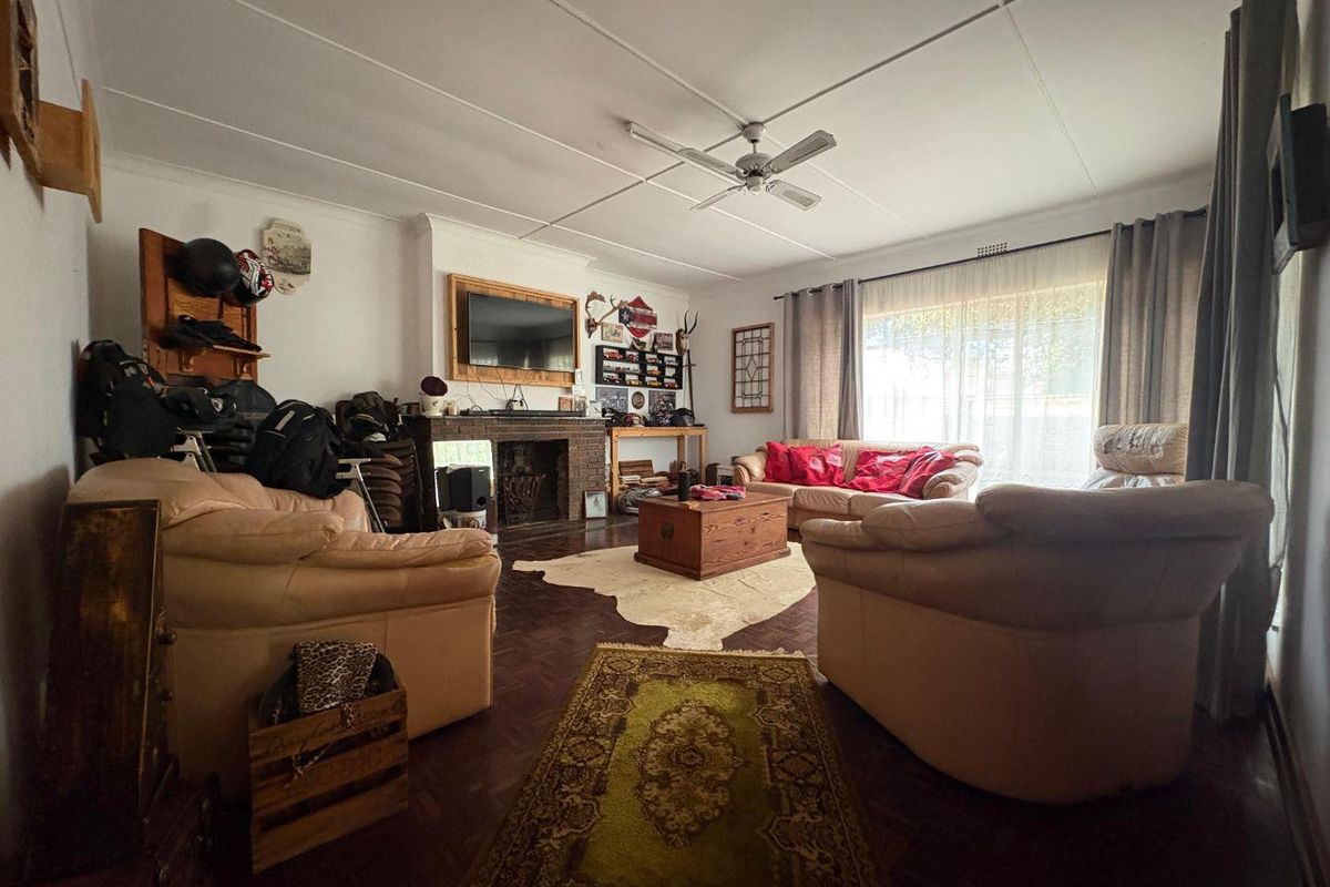 Spacious living room featuring classic parquet flooring, a brick fireplace, and a ceiling fan, offering a comfortable and traditional living space.