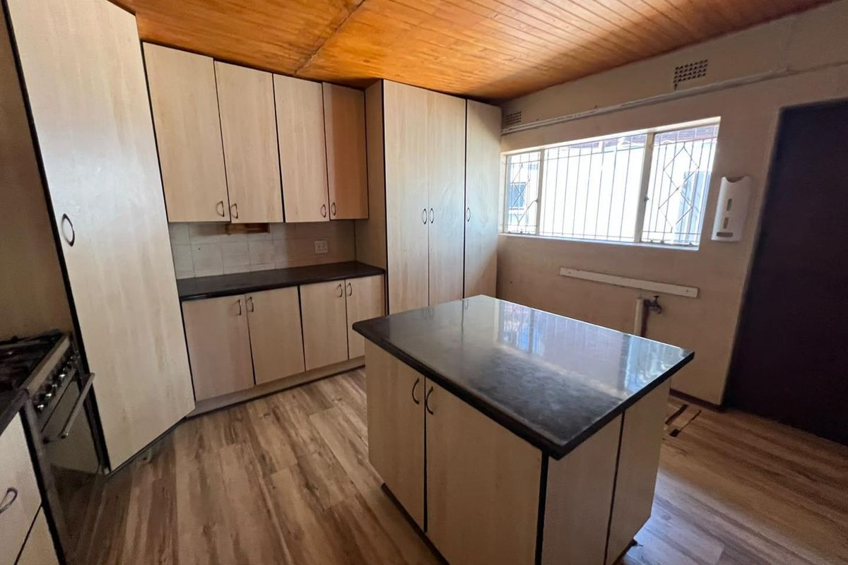 A functional kitchen featuring light wood-tone cabinetry, a central island with a dark countertop, timber ceiling, and laminate flooring.