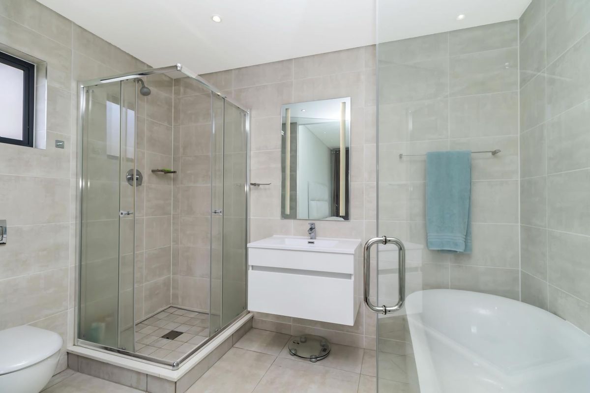 Modern bathroom featuring a glass-enclosed shower, a separate bathtub, a wall-mounted vanity with basin, and neutral floor-to-ceiling tiling.