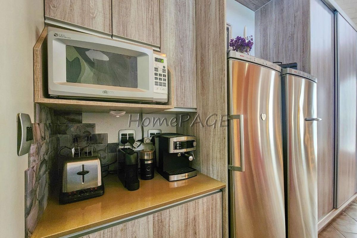 A compact kitchen area featuring wood-grain cabinetry, a built-in microwave, stone-look backsplash, and space for a side-by-side refrigerator.