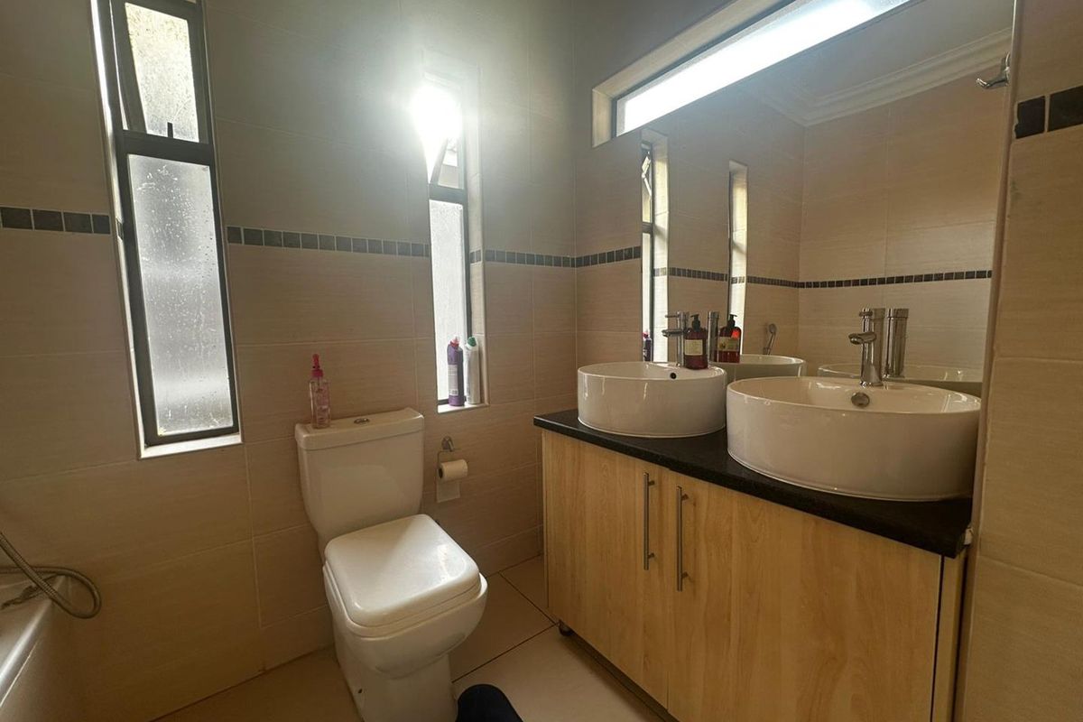 A functional bathroom featuring a double vanity with vessel sinks, a toilet, and tiled walls with a decorative border.