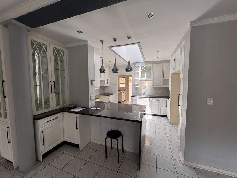 A well-lit kitchen featuring white cabinetry, granite countertops, a central breakfast bar, and a skylight, providing a functional and bright workspace.