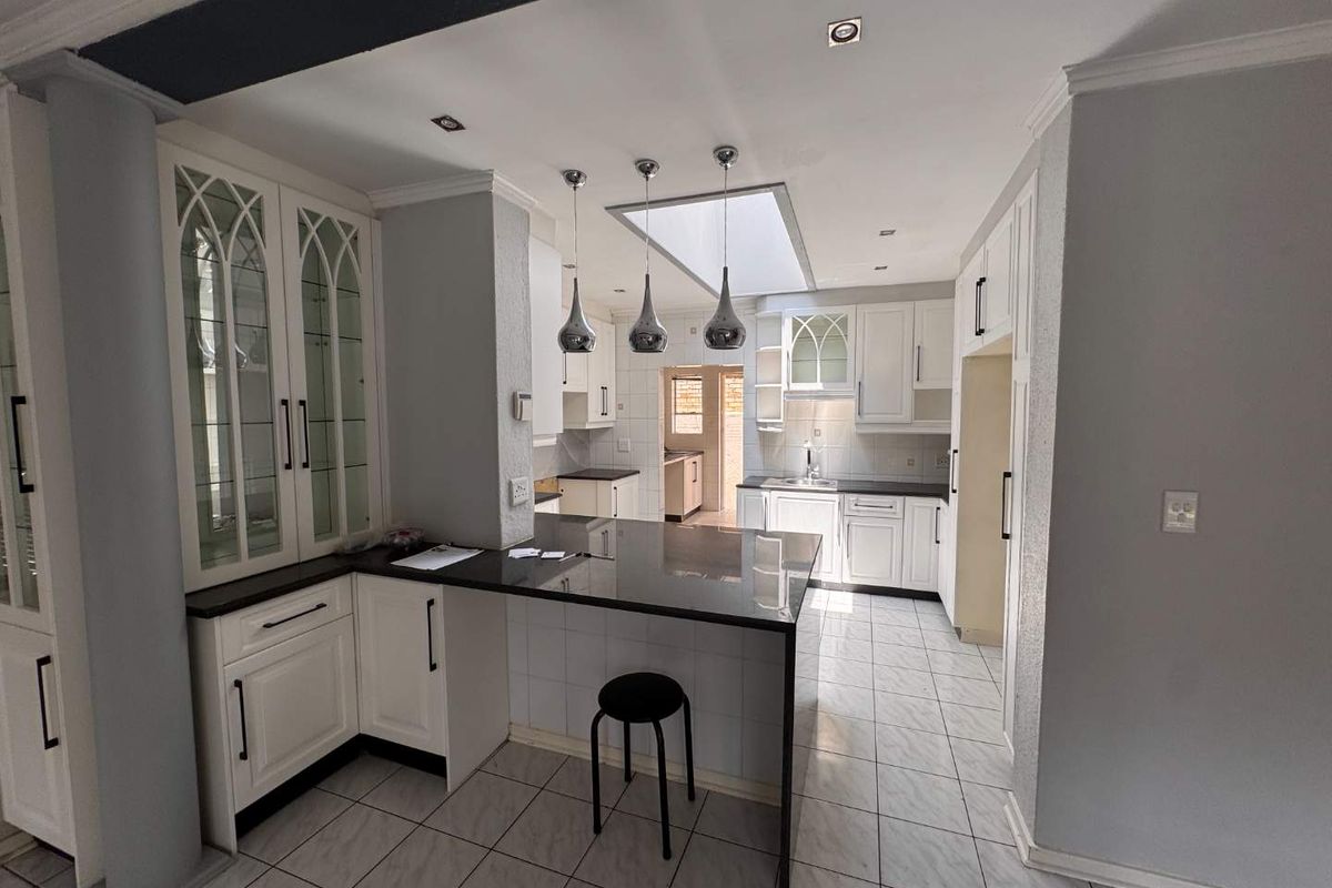 A well-lit kitchen featuring white cabinetry, granite countertops, a central breakfast bar, and a skylight, providing a functional and bright workspace.