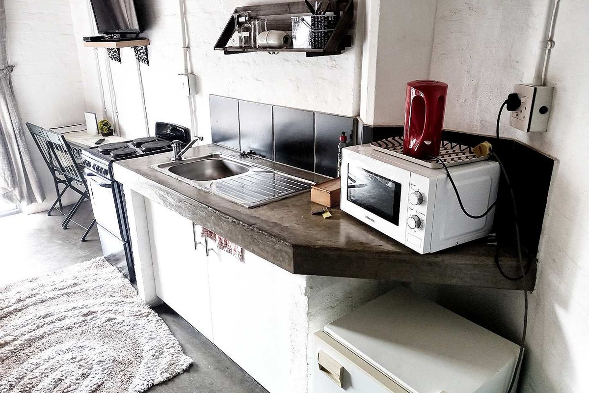 Compact kitchen area featuring a concrete countertop, stainless steel sink, and built-in stove, set against a rustic white-painted brick wall.