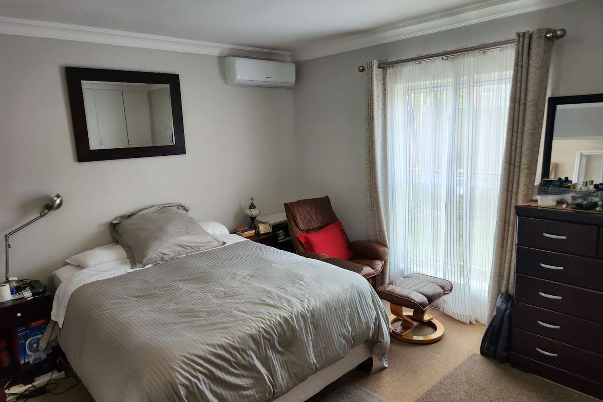 A comfortable bedroom featuring a wall-mounted air conditioning unit and a sliding glass door providing access to the exterior.
