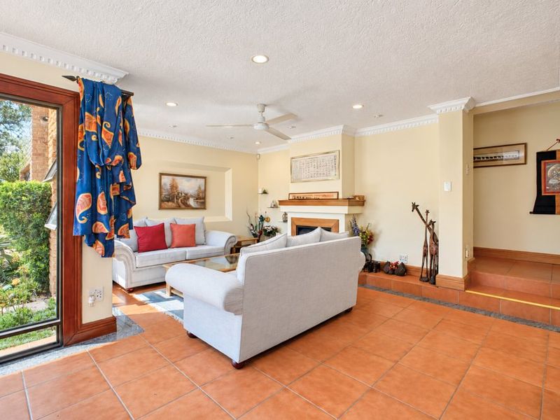 Spacious living room featuring terracotta floor tiles, a fireplace, crown molding, and large sliding glass doors providing natural light and garden access.