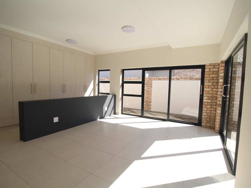 A bright, modern living space featuring extensive built-in cabinetry, large sliding glass doors, and stylish exposed brick accents with neutral tiled flooring.