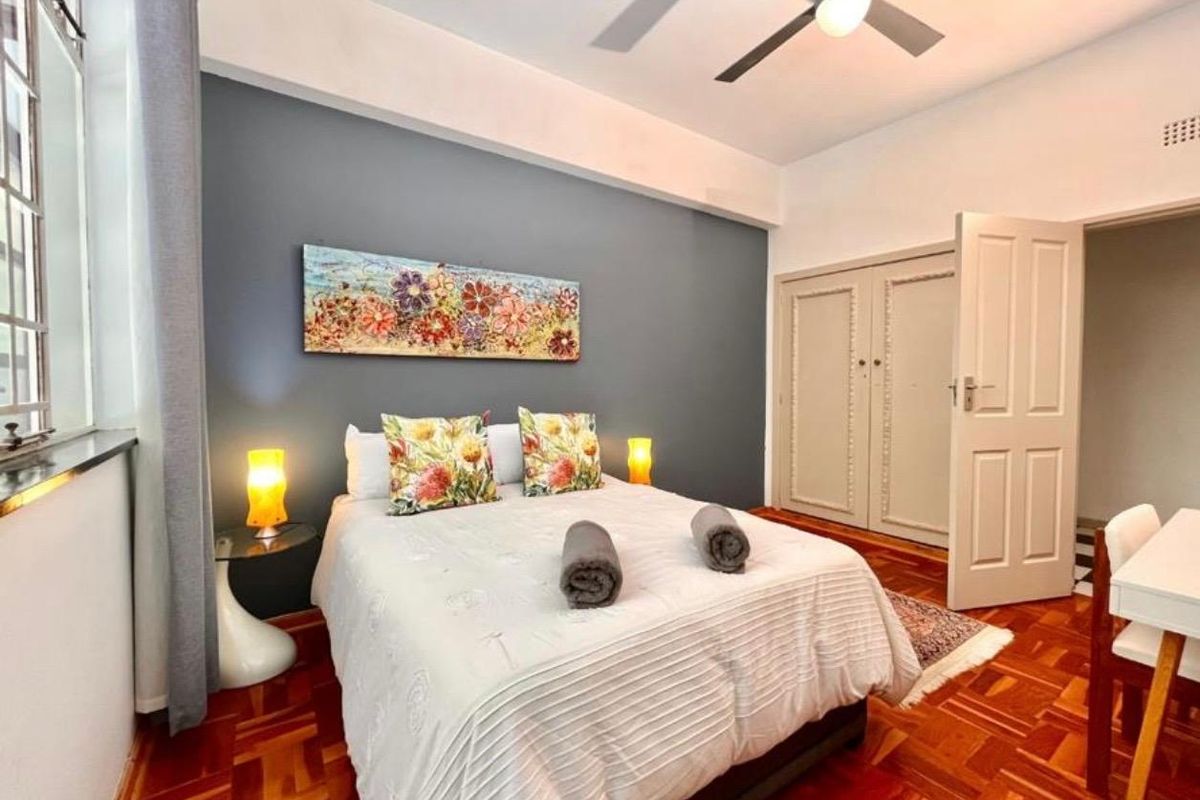 A well-maintained bedroom featuring classic parquet flooring, a built-in wardrobe, and a ceiling fan, offering a comfortable and functional living space.