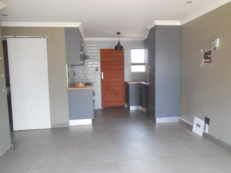 A compact, modern kitchen featuring grey cabinetry, subway tile backsplash, and timber-look countertops, currently vacant and awaiting final electrical finishing touches.
