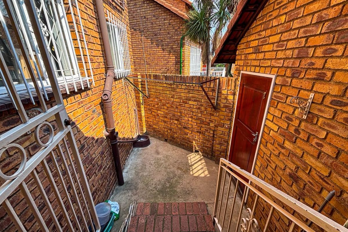 A private rear courtyard area featuring face brick walls, secure metal gates, and concrete flooring, providing a functional outdoor utility space.