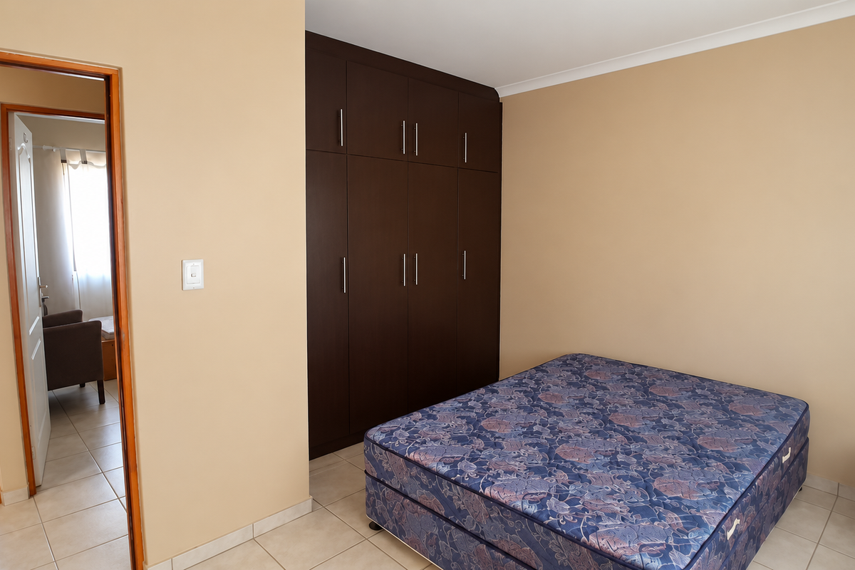 A bedroom featuring dark wood built-in cupboards, neutral wall paint, and tiled flooring, with an adjacent view into a bathroom area.
