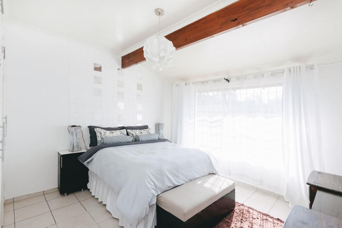 A bright bedroom featuring tiled flooring, a decorative textured feature wall, and an exposed timber ceiling beam.