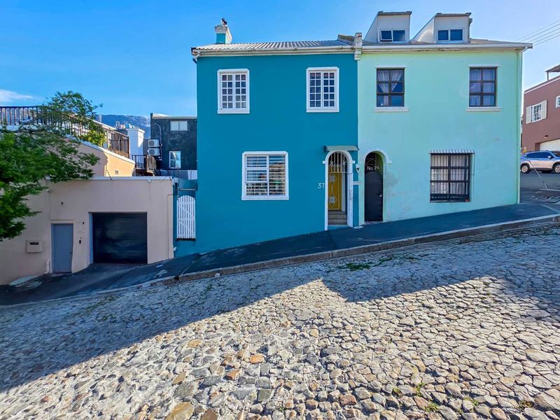 A vibrant, multi-colored terraced house featuring a garage, dormer windows, and secure entrance, situated on a historic cobblestone street.