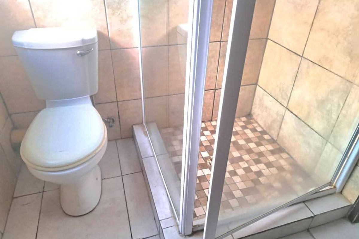 A functional bathroom featuring a standard toilet and a glass-enclosed shower with tiled finishes throughout.