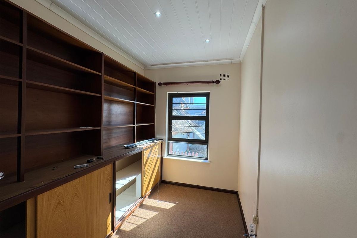 A functional study or bedroom featuring extensive built-in wooden shelving and cabinetry, neutral walls, and a tongue-and-groove ceiling with recessed lighting.