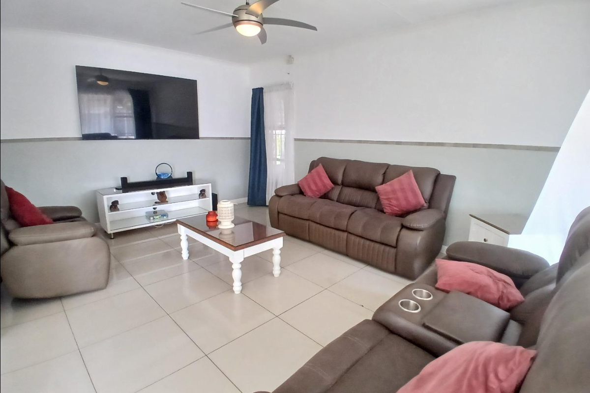 A spacious living room featuring large floor tiles, a ceiling fan, and a wall-mounted television, offering a comfortable and functional family area.